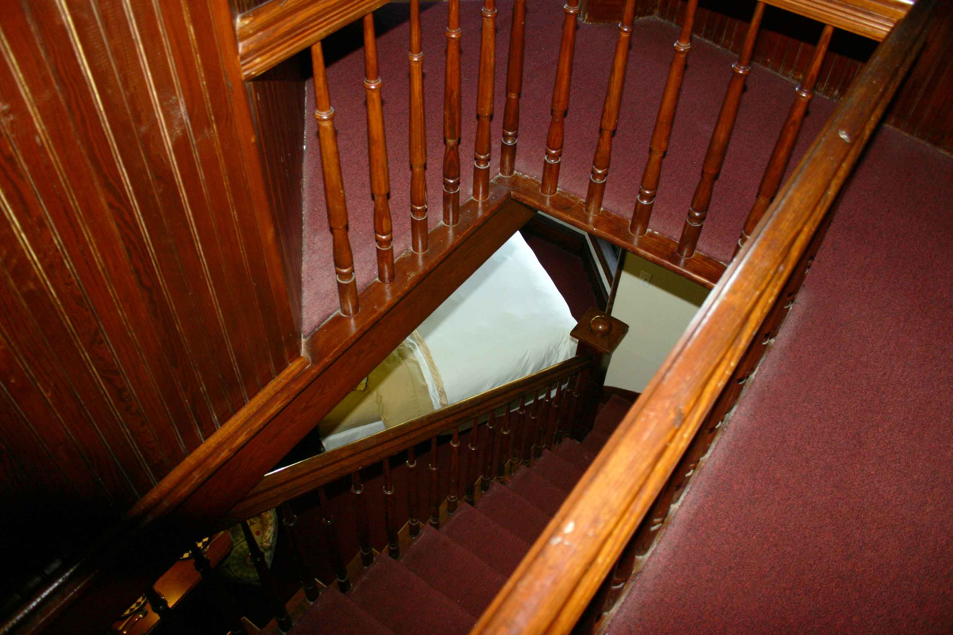 A wooden staircase with red carpet and wood railing.